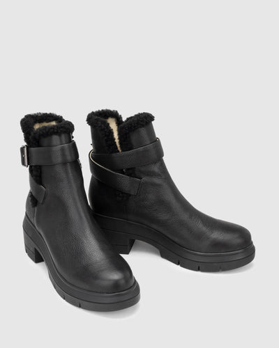 Chaos & Harmony Broadway Boot in black is a comfortable slip on leather boot.  There is black shearling around the top of the boot and the wrap around strap sits around the ankle. Black leather boot with shearling detail and buckle Soft leather lined Black rubber mould outsole