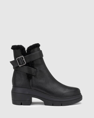 Chaos & Harmony Broadway Boot in black is a comfortable slip on leather boot.  There is black shearling around the top of the boot and the wrap around strap sits around the ankle. Black leather boot with shearling detail and buckle Soft leather lined Black rubber mould outsole
